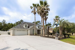 A two-story house with a garage, surrounded by palm trees and a well-maintained lawn.
