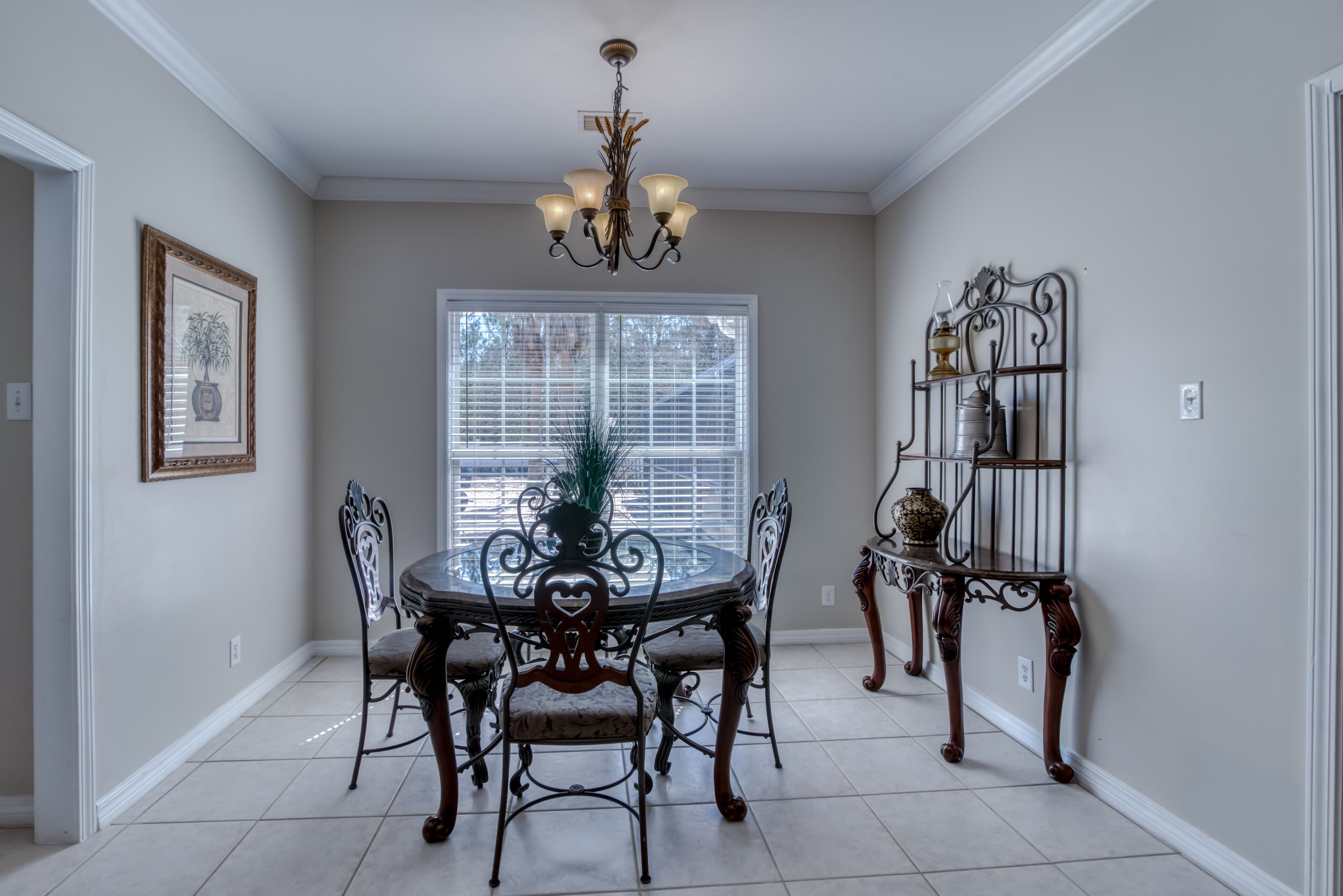 A dining area with a round table, six chairs, a chandelier, a potted plant, and a decorative metal shelf.