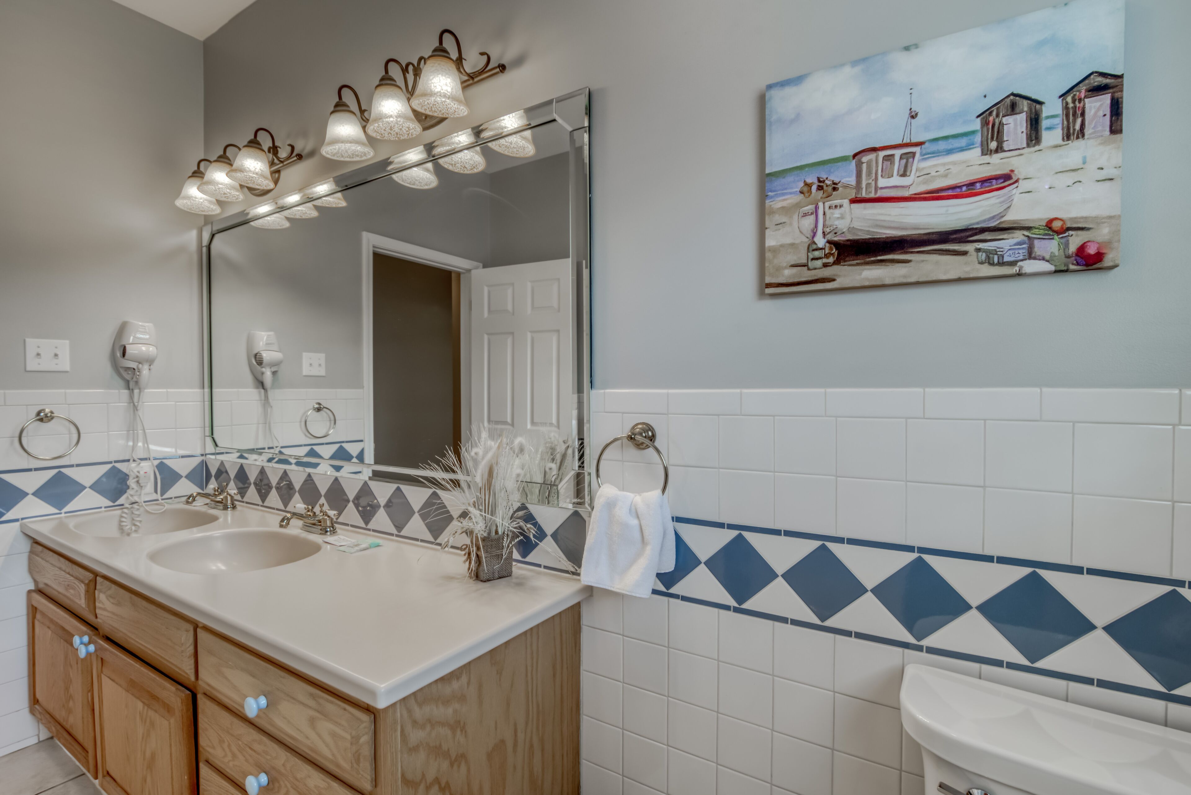 Une salle de bain avec un meuble-lavabo à deux vasques, un grand miroir et un tableau représentant une scène de plage.