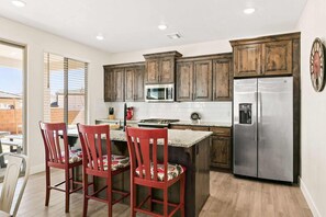 A kitchen with wooden cabinets, a stainless steel refrigerator, and a bar area with red chairs.