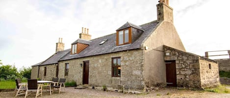 A stone house with a gravel driveway, a wooden table, and two chairs.