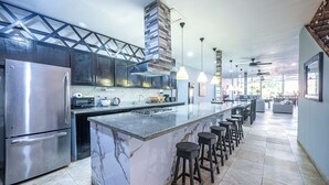 A modern kitchen with a stainless steel refrigerator, marble countertops, a central island with bar stools, and pendant lighting. - Party like a King, Close to Jaco Center in the ultimate party pad!        (Jacó)