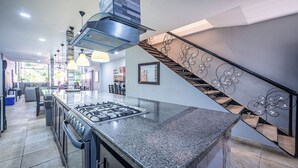 A modern kitchen with a granite countertop, stainless steel appliances, and a staircase with decorative railings. - Party like a King, Close to Jaco Center in the ultimate party pad!        (Jacó)