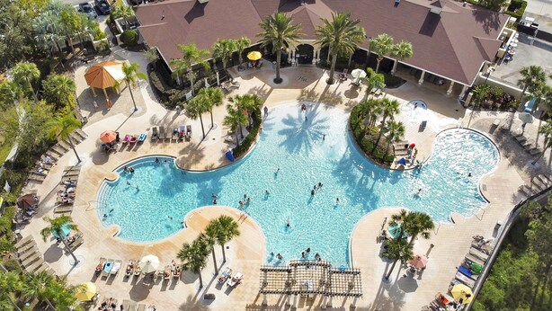 Eine Luftaufnahme eines Resorts mit einem großen zentralen Pool, mehreren Liegebereichen und Palmen.