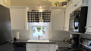 A kitchen with white cabinets, a black refrigerator, a stove, and a coffee maker. - Historic Bungalow in the Heart of the City (Mission,)