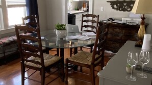 A dining area with a glass table, wooden chairs, and a laptop. There is a kitchen visible through an open door. - Historic Bungalow in the Heart of the City (Mission,)
