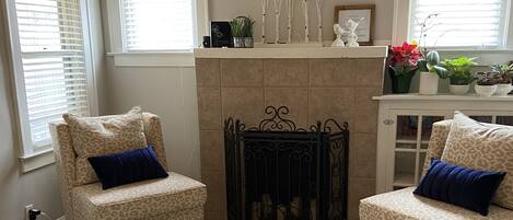 A living room with two leopard print armchairs, a white coffee table, a fireplace, and a bookshelf with plants.