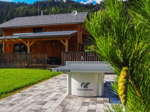 Una cabaña de madera con un  área de estar al aire libre techada, una mesa de ping pong y un césped bien cuidado.