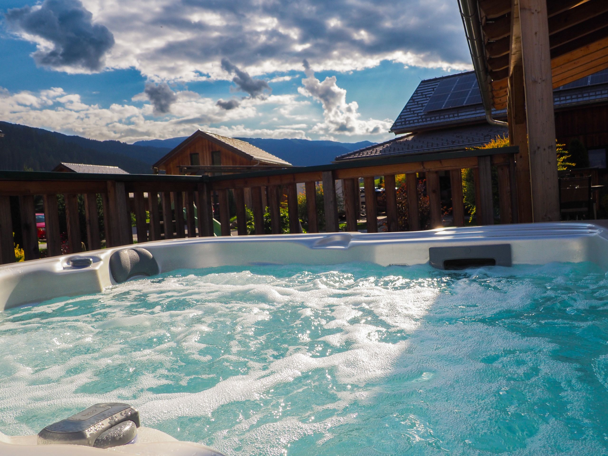 A hot tub with a wooden deck and a mountain backdrop.