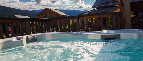 A hot tub with a wooden deck and a mountain backdrop.