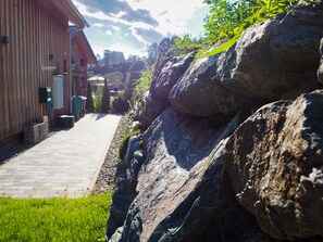A pathway leading to a building with a wooden exterior, surrounded by large rocks and greenery.