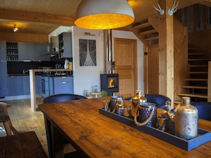 A wooden dining table with a tray of bottles and glasses, a wooden ceiling, a kitchen with blue cabinets, and a fireplace. - Murau 18 - Chalet with whirlpool & infrared sauna (Murau)