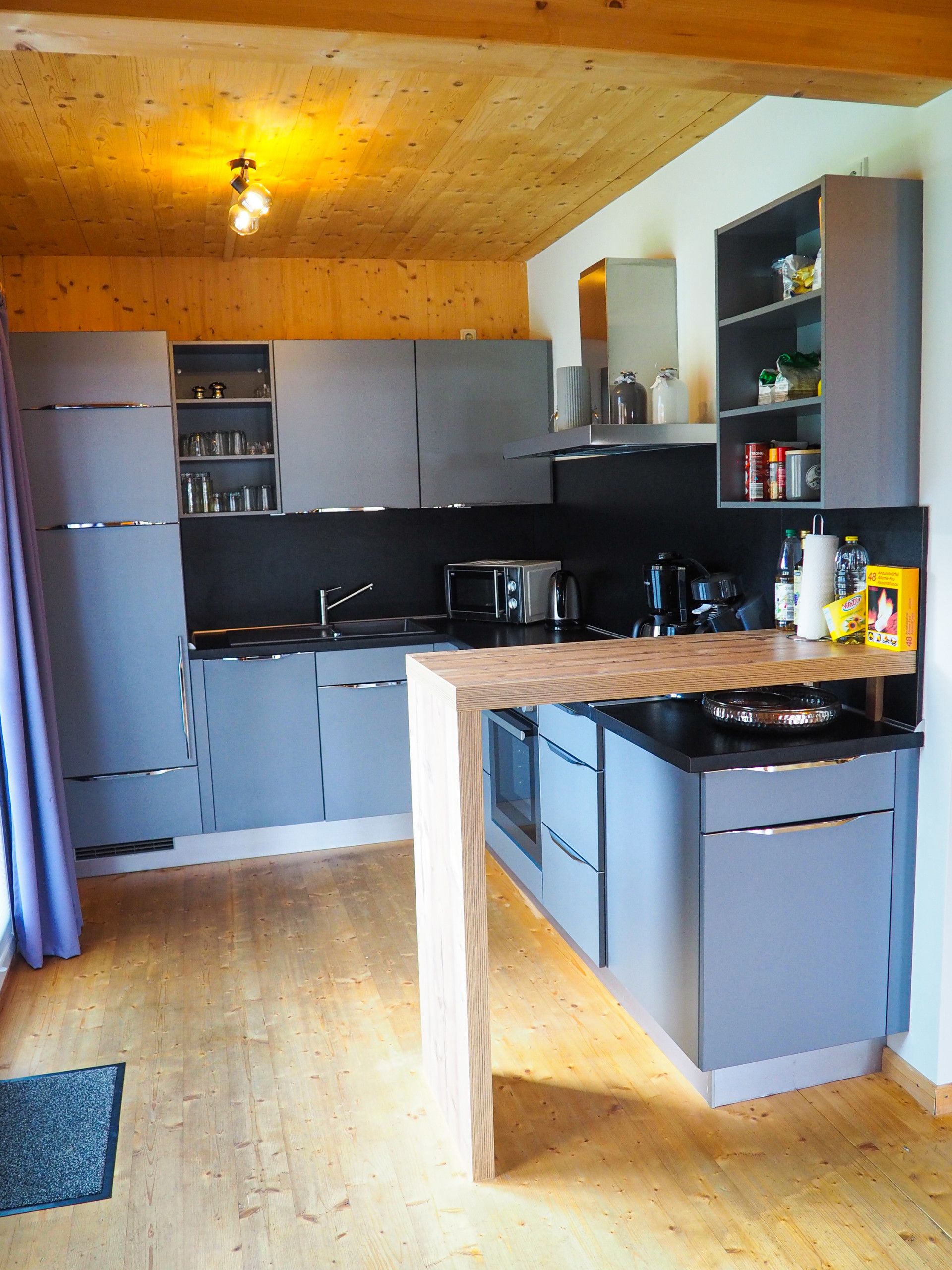 Eine moderne Küche mit grauen Schränken, einer Holz Arbeitsplatte und einem eingebauten Backofen.
