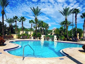 A swimming pool with a curved edge, surrounded by palm trees and lounge chairs. - Cozy Studio - 20 minutes from Disney - LOWEST price in Regal Palms Resort (Davenport)