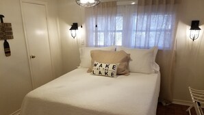 Ein Schlafzimmer mit Bett, einem Fenster mit durchsichtigen Vorhängen und Wandleuchten.