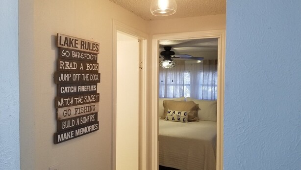 Ein Zimmer mit einem Bett und einem an der Wand befestigten Schild, das 'LAKE RULES' mit Aktivitäten wie 'BARFOOT GEHEN' und 'EIN BUCH LESEN' aufführt.