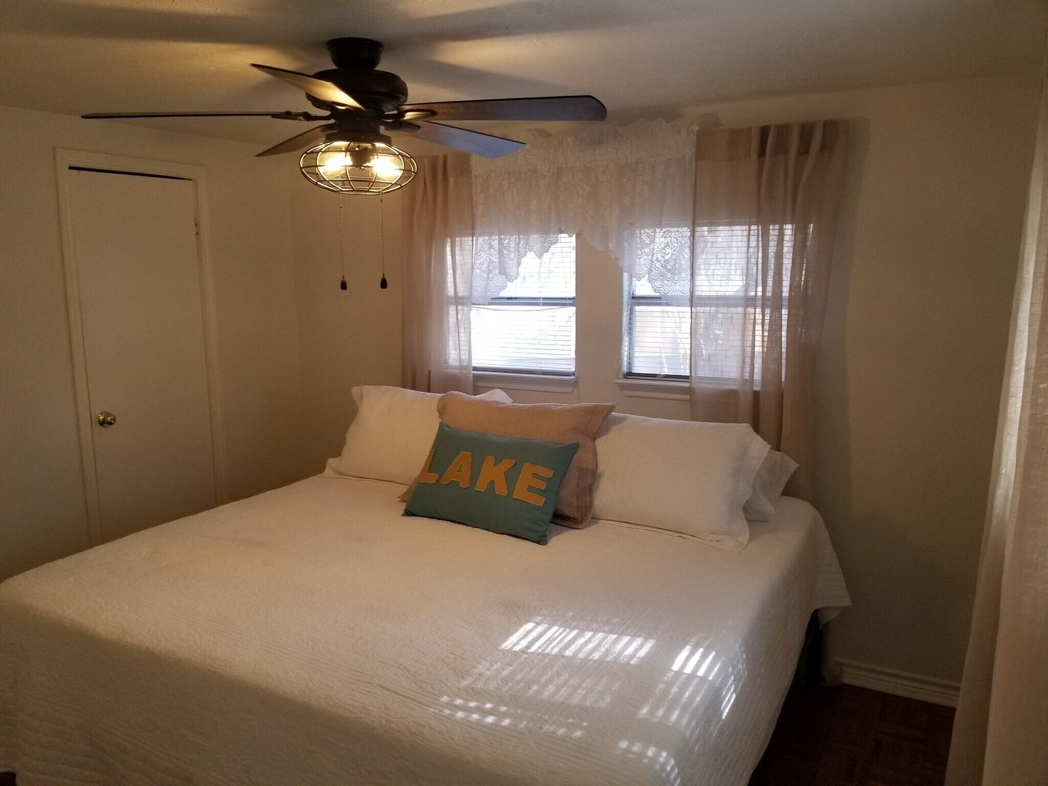 Un dormitorio con una cama, ventilador de techo y ventana con cortinas.