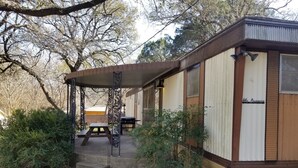 Ein kleines, einstöckiges Gebäude mit überdachter Terrasse, einem Picknicktisch und einem Grill.