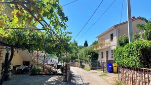 Una calle soleada con viñedos, edificios de piedra y cielo despejado.