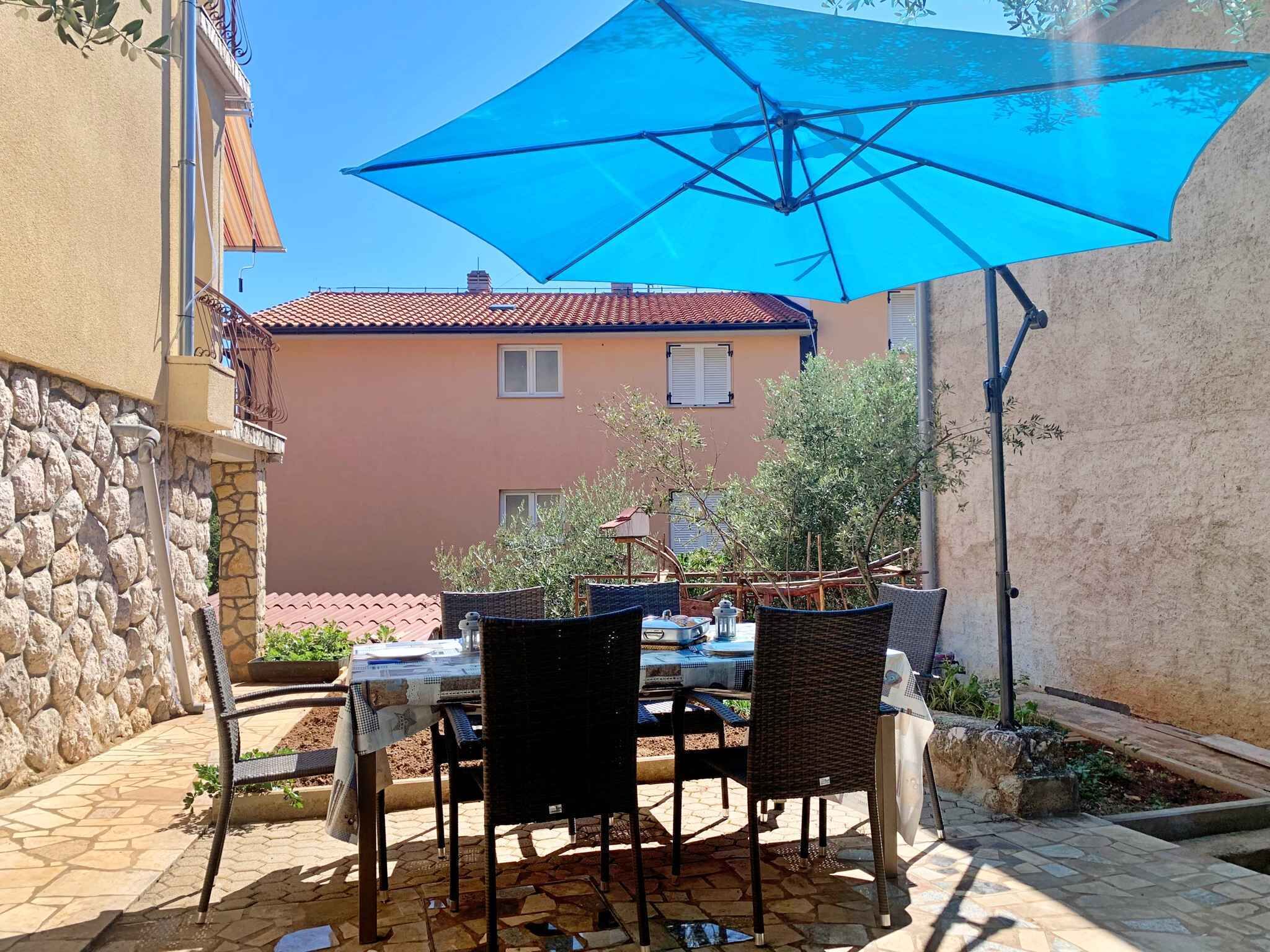 Un patio al aire libre con una mesa, sillas, un paraguas azul y un muro de piedra.