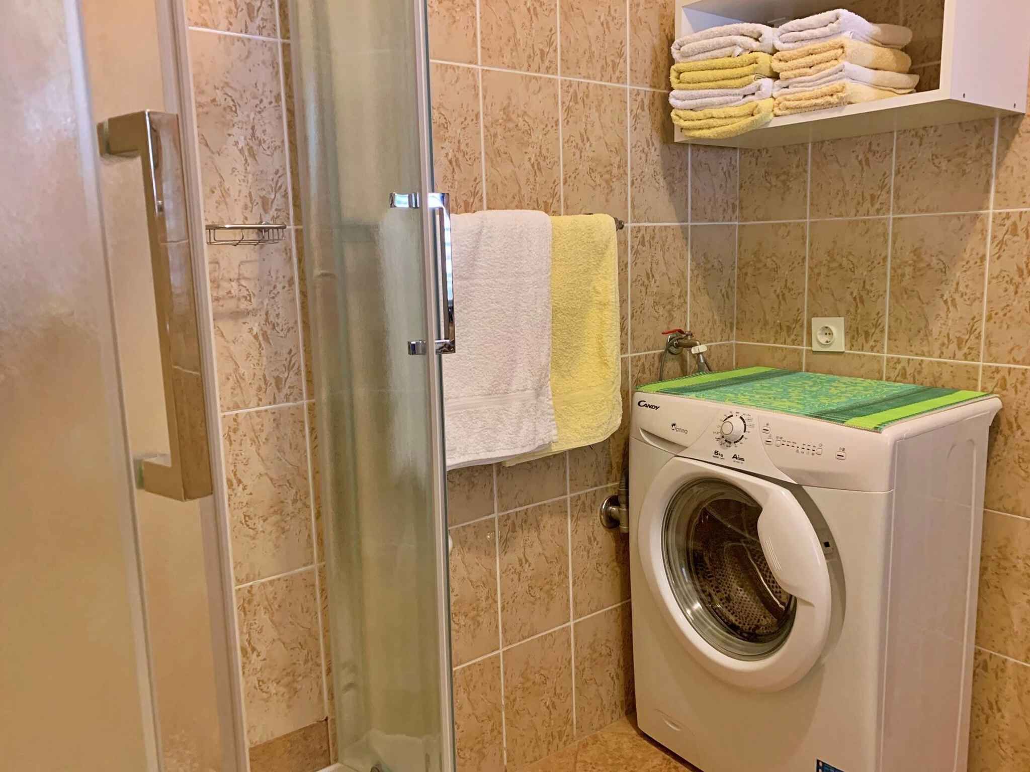Een badkamer met een douchecabine van glas, een wasmachine en een handdoekrek met opgevouwen handdoeken.