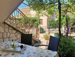 Eine Terrasse im Freien mit Esstisch, Steintreppe zu einem Balkon und Blick auf eine Wohngegend.