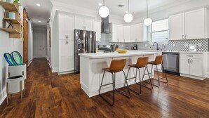 Une cuisine moderne avec des meubles blancs, un îlot central doté de tabourets de bar, un réfrigérateur en acier inoxydable et un crédence carrelée en noir et blanc.