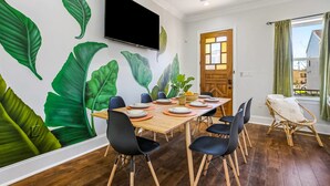 Un coin repas avec une table en bois, dressée pour quatre personnes, entourée de chaises noires. Un téléviseur à écran plat est fixé au mur, au-dessus de la table.