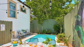 Un jardin avec une piscine, un espace salon extérieur et une table dressée pour un repas.