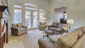 A spacious living room with a high ceiling, large windows, and a view of the outdoors. There are two sofas, a coffee table, and a lamp.