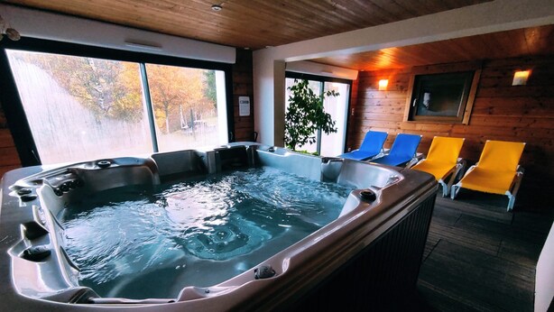 A hot tub with four chairs, a wooden interior, and a view of trees through large windows. - A L'orée du Bois (Dommartin-lès-Remiremont)