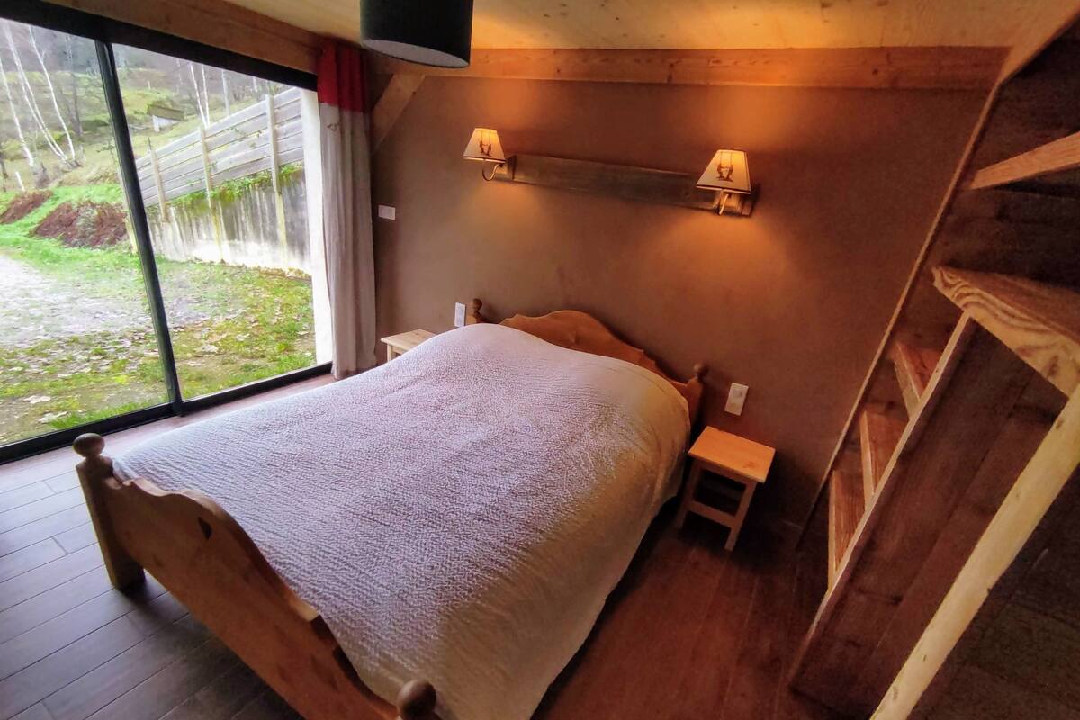 A wooden-framed bedroom with a large bed, two bedside tables, and a window offering a view of the outdoors.