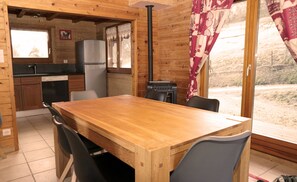 A wooden interior with a dining table, chairs, a kitchen area, and a large window with curtains. - A L'orée du Bois (Dommartin-lès-Remiremont)