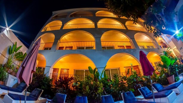 A multi-story hotel with balconies, outdoor seating, and potted plants. - Hotel Delfin (Barra de Navidad)