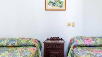 Habitació amb dos llits, cadascun amb una colcha de disseny floral, una petita taula de nit de fusta entre ells, i un quadre amb marc a la paret.