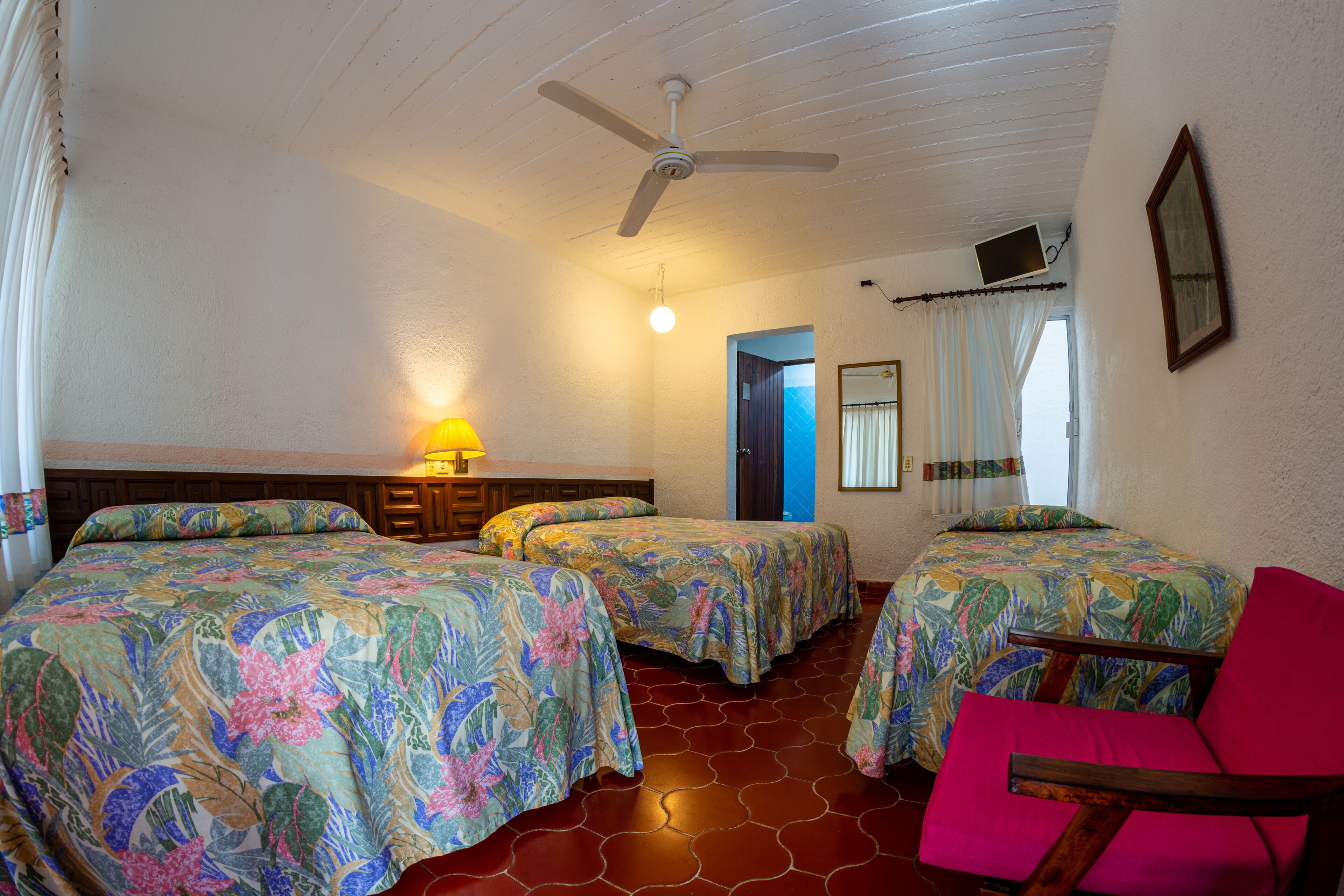 A hotel room with three beds, a ceiling fan, a TV, and a window with curtains.