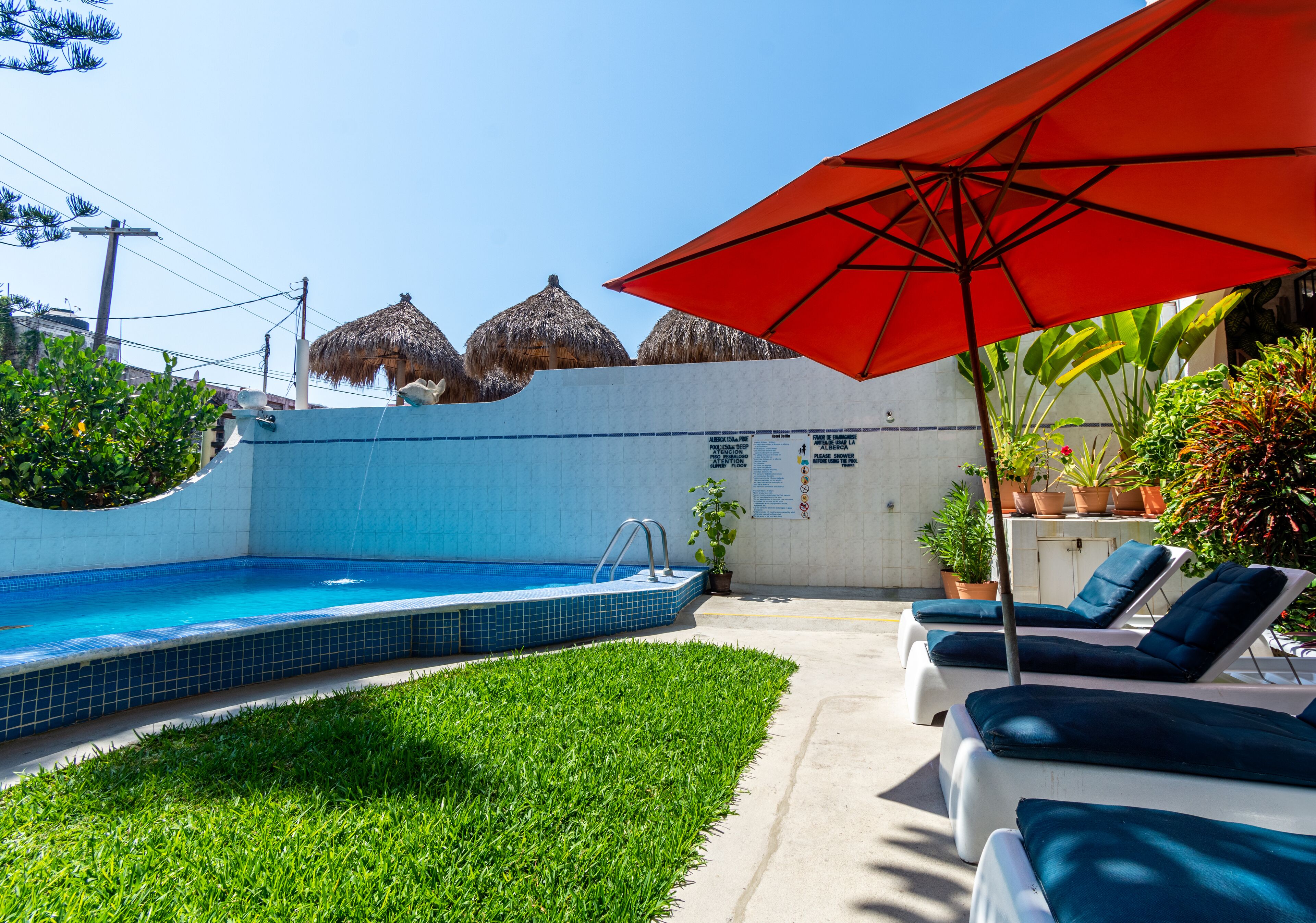 Una piscina con un pequeño solárium, sillas de descanso y una sombrilla roja.