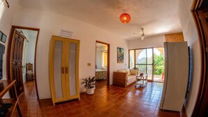 A spacious living area with a tiled floor, a wooden cabinet, a potted plant, a sofa, and a refrigerator. - Hotel Delfin (Barra de Navidad)