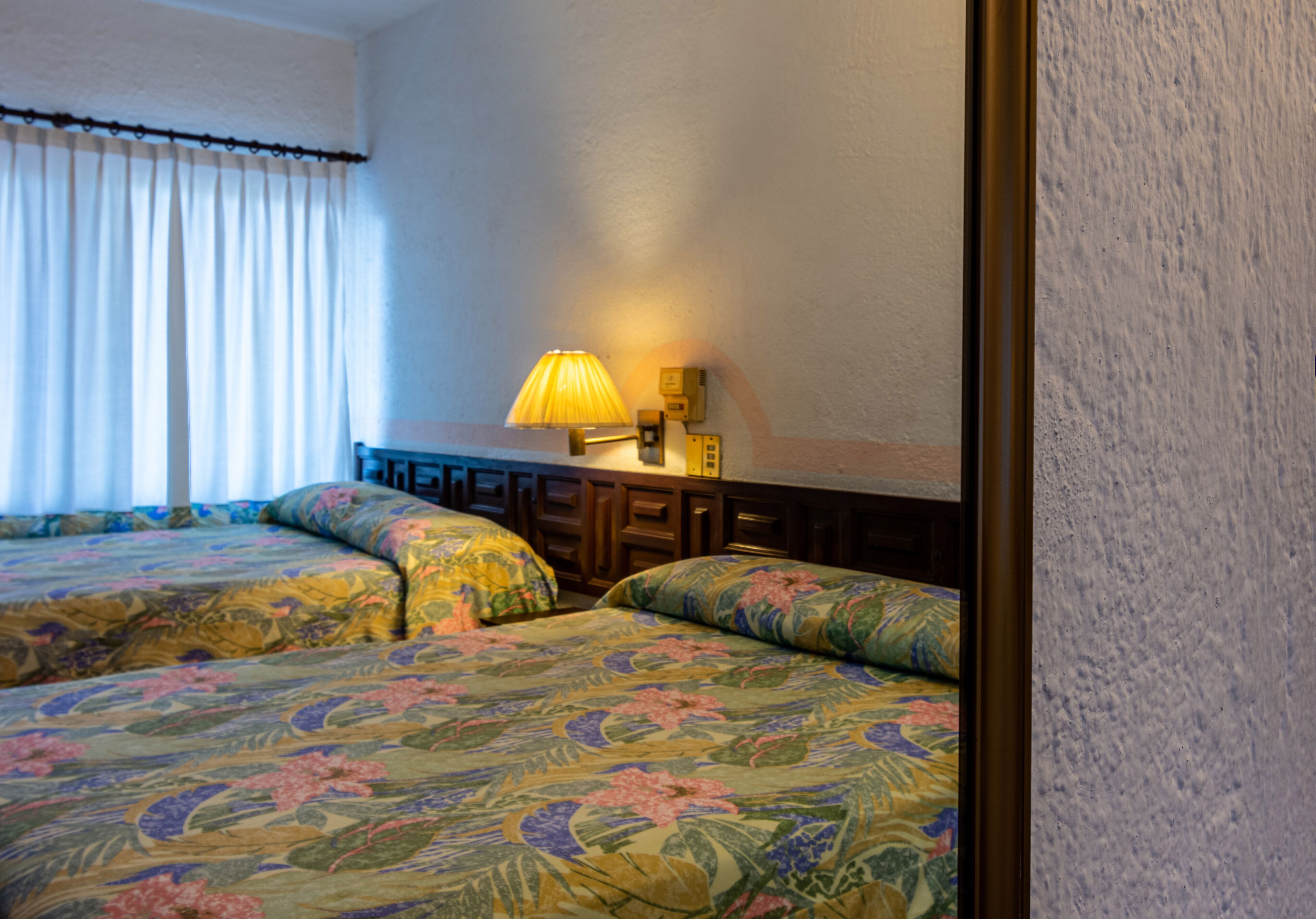 A hotel room with two beds, a nightstand, a lamp, and a wall-mounted telephone.