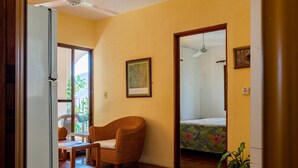 A room with a wicker chair, a bed with a floral bedspread, a ceiling fan, and a framed picture on the wall. - Hotel Delfin (Barra de Navidad)