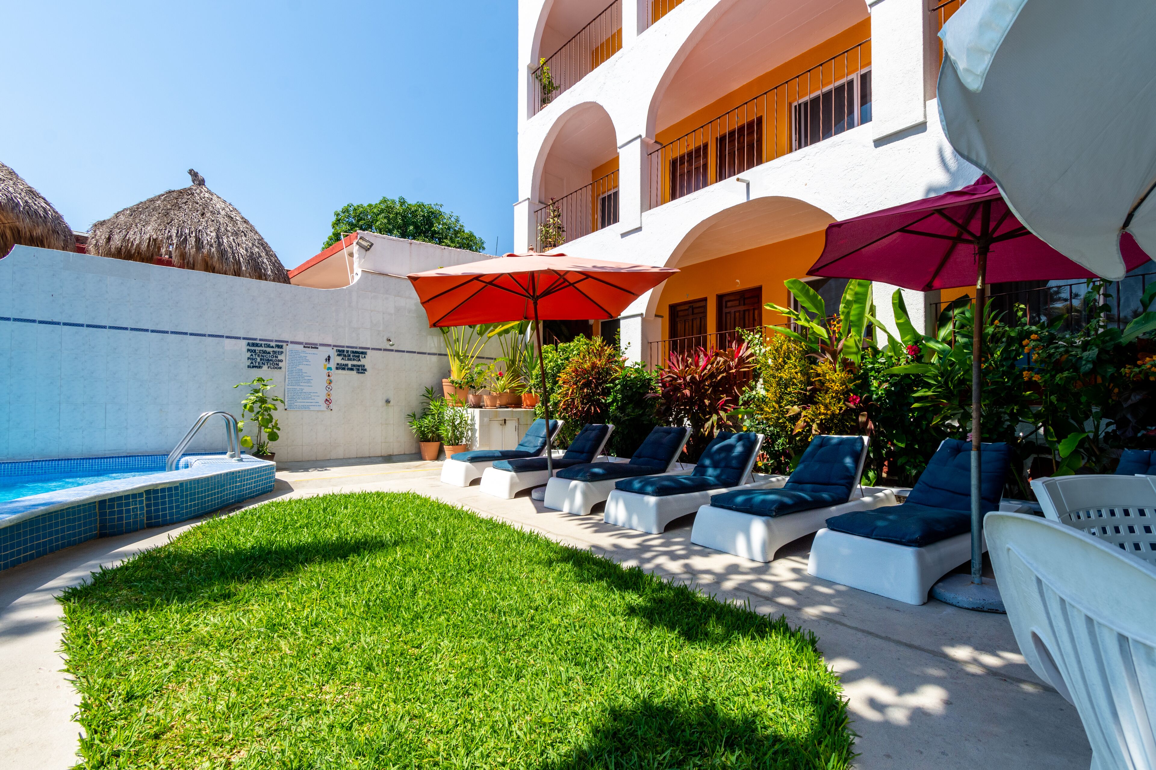 A pool area with lounge chairs and umbrellas, a swimming pool, and a building with balconies.