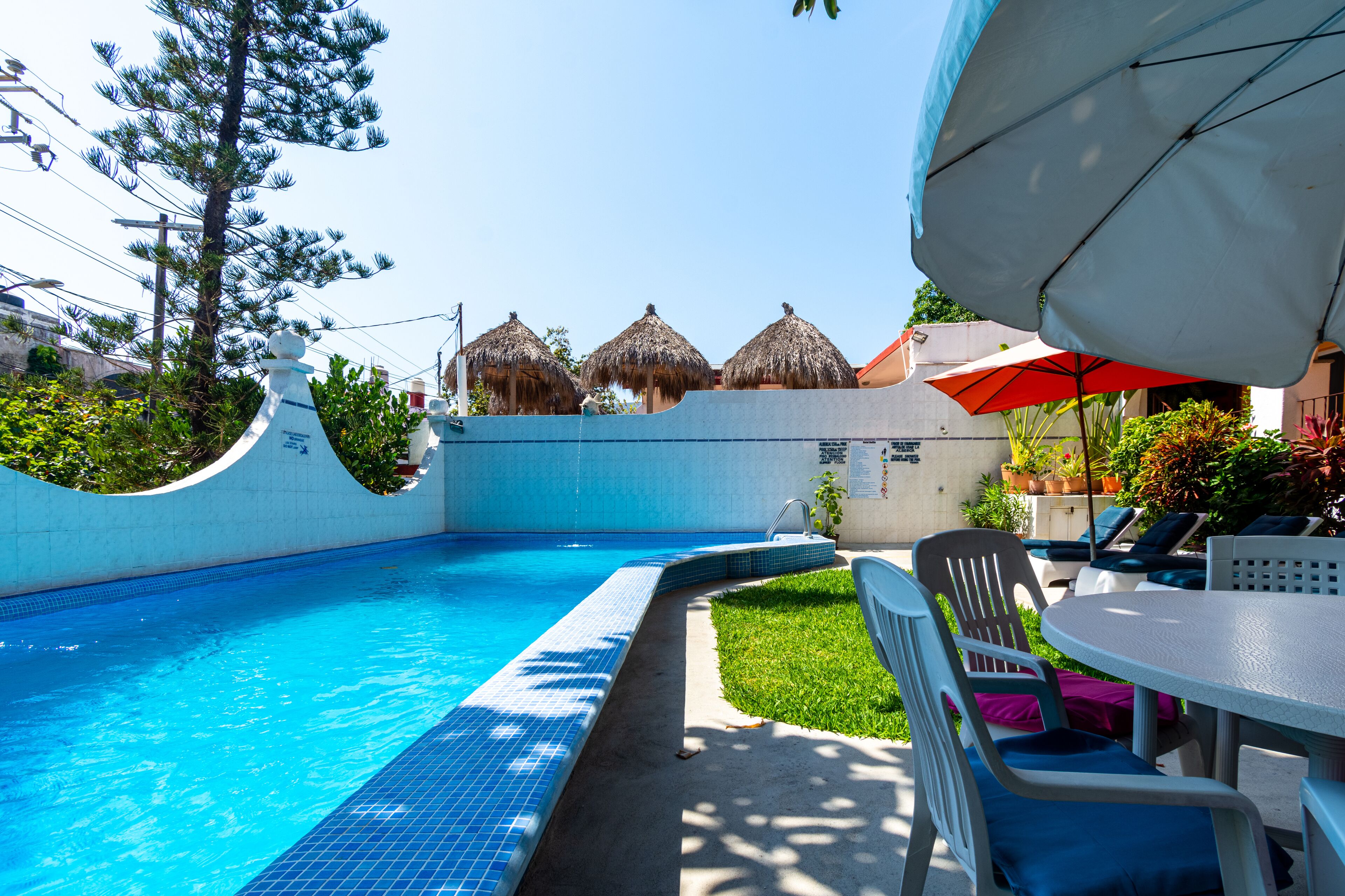 A swimming pool with a tiled edge, a grassy area, and a table with chairs.