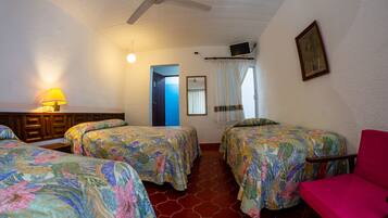 A room with two beds, a chair, a ceiling fan, a lamp, and a TV on the wall.