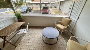 Une terrasse couverte avec une table, des chaises et une vue sur la rue.
