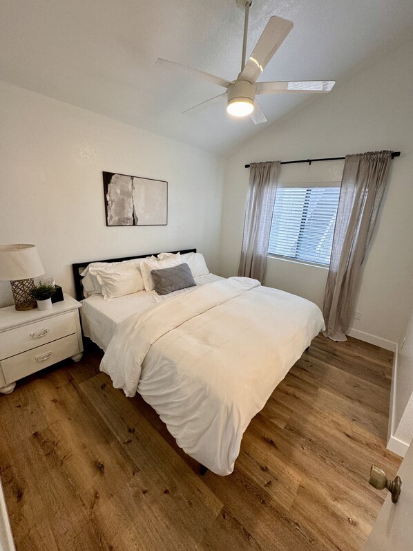 A bedroom with a bed, nightstand, ceiling fan, window with curtains, and a wall-mounted abstract painting. - Downtown Gilbert Gem - Recently Updated (Gilbert)