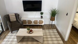 Un salon comprenant un canapé, une table basse, un téléviseur à écran plat, une plante et un petit meuble.