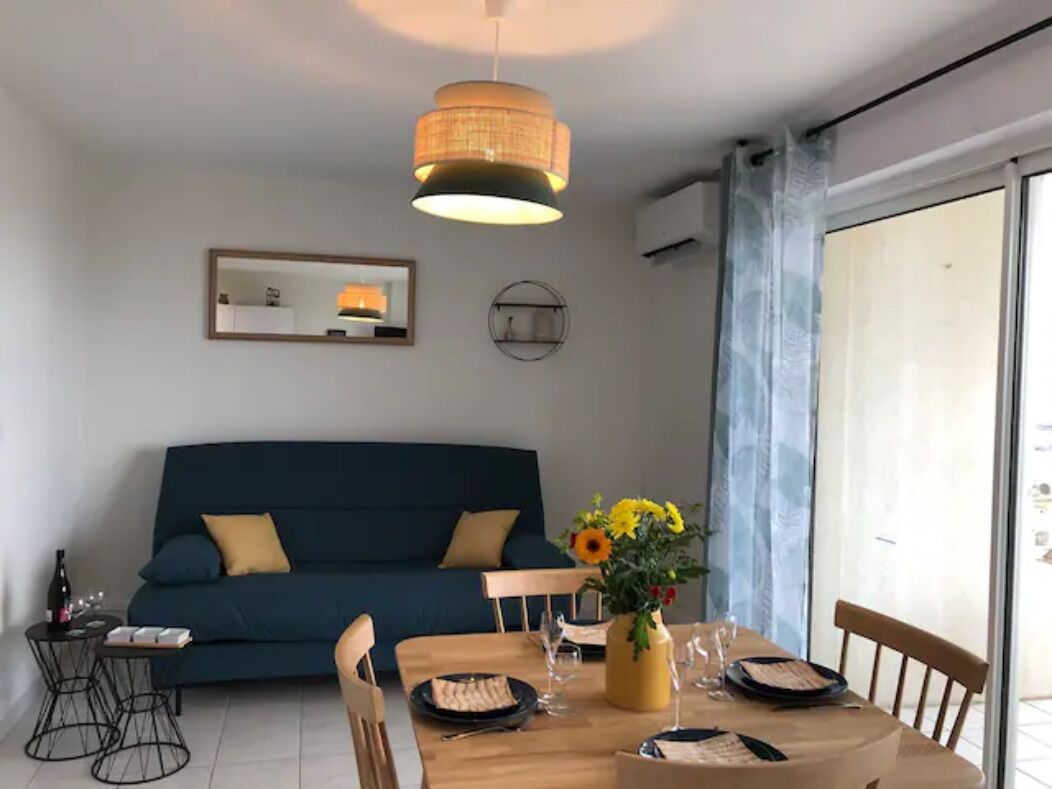 Een moderne woonkamer met een blauwe bank, een houten eettafel voor twee personen en een hanglamp.