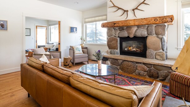 A cozy living room with a stone fireplace, leather sofa, and a glass coffee table. - Big Sky Escape - Spacious Home with Hot Tub (Big Sky)