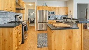 A modern kitchen with wooden cabinets, stainless steel appliances, and a black countertop island. - Big Sky Escape - Spacious Home with Hot Tub (Big Sky)