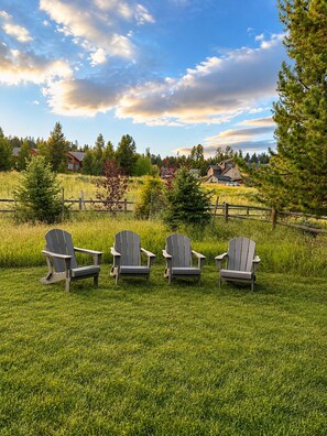 Un champ herbeux avec trois chaises Adirondack et une clôture en bois.